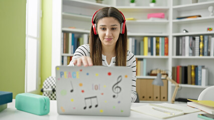 Young beautiful hispanic woman student using laptop and headphones studying at library university