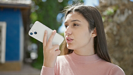Young beautiful hispanic woman sending voice message with smartphone at park