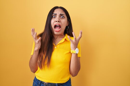 Young arab woman standing over yellow background crazy and mad shouting and yelling with aggressive expression and arms raised. frustration concept.