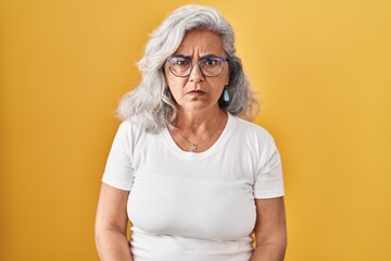 Middle age woman with grey hair standing over yellow background skeptic and nervous, frowning upset because of problem. negative person.