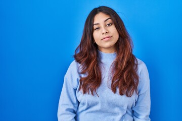 Hispanic young woman standing over blue background looking sleepy and tired, exhausted for fatigue and hangover, lazy eyes in the morning.