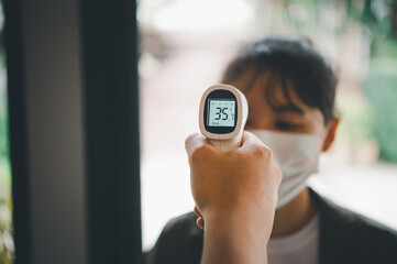 Hand holding infrared thermometer to measuring temperature  people with face mask on background. Covid flu screening 19 concept. - obrazy, fototapety, plakaty