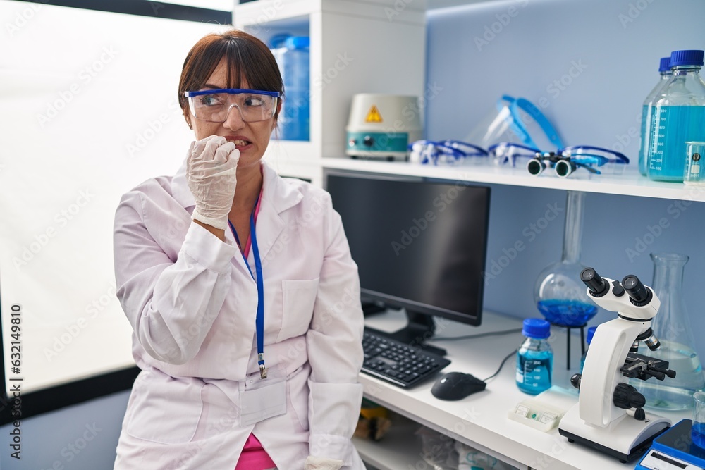 Sticker Young brunette woman working at scientist laboratory looking stressed and nervous with hands on mouth biting nails. anxiety problem.