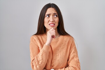 Young brunette woman standing over white background thinking worried about a question, concerned and nervous with hand on chin