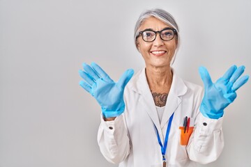 Middle age woman with grey hair wearing scientist robe showing and pointing up with fingers number nine while smiling confident and happy.