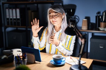 Middle age woman with grey hair working at the office at night showing and pointing up with fingers number six while smiling confident and happy.