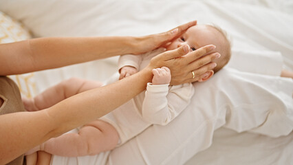 Mother and daughter sitting on bed together touching face at bedroom