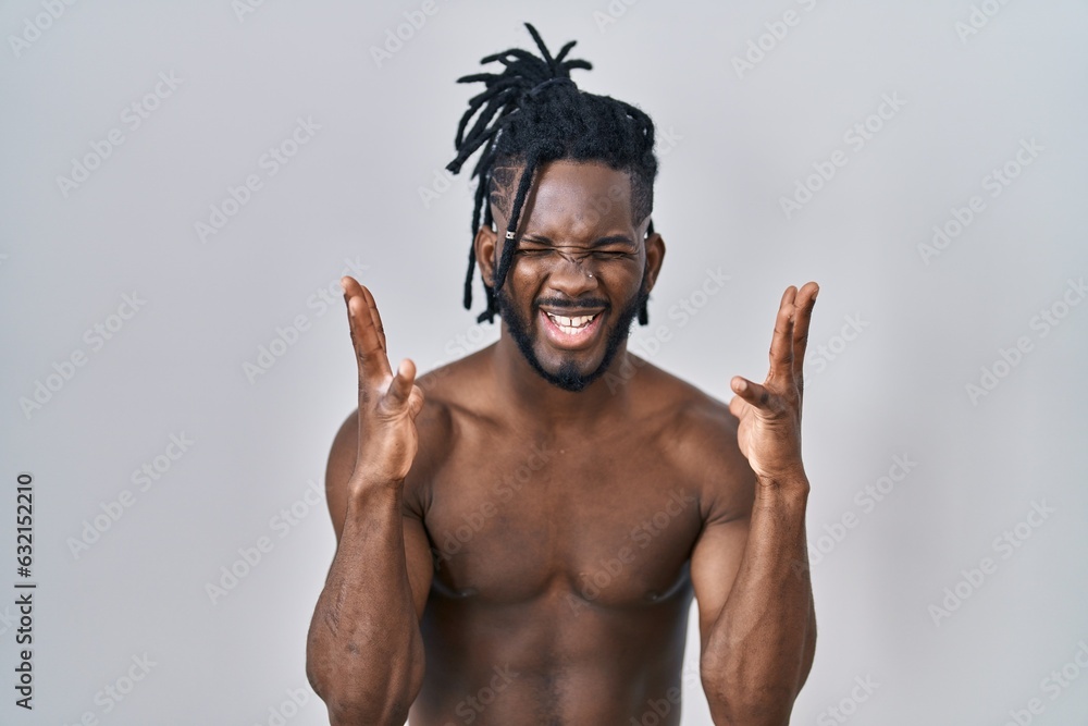 Poster African man with dreadlocks standing shirtless over isolated background celebrating mad and crazy for success with arms raised and closed eyes screaming excited. winner concept