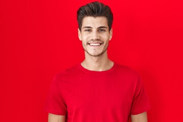 Young hispanic man standing over red background with a happy and cool smile on face. lucky person.