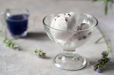 Lavender ice cream in a glass bowl, lavender syrup in a jug, lavender branches over grey concrete background