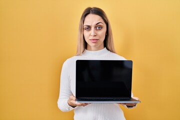 Young blonde woman holding laptop skeptic and nervous, frowning upset because of problem. negative...