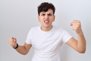 Young non binary man wearing casual white t shirt angry and mad raising fists frustrated and furious while shouting with anger. rage and aggressive concept.