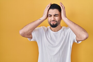 Fototapeta na wymiar Young handsome man wearing casual t shirt over yellow background suffering from headache desperate and stressed because pain and migraine. hands on head.
