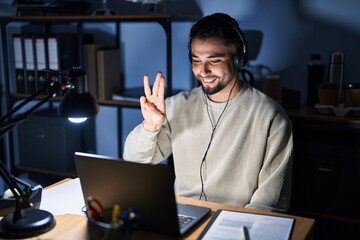 Young handsome man working using computer laptop at night showing and pointing up with fingers number three while smiling confident and happy.