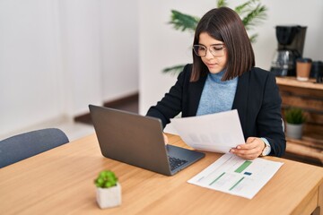 Young beautiful hispanic woman business worker using laptop reading document at office