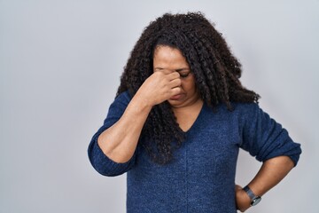 Plus size hispanic woman standing over white background tired rubbing nose and eyes feeling fatigue and headache. stress and frustration concept.