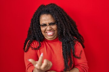 Plus size hispanic woman standing over red background beckoning come here gesture with hand inviting welcoming happy and smiling