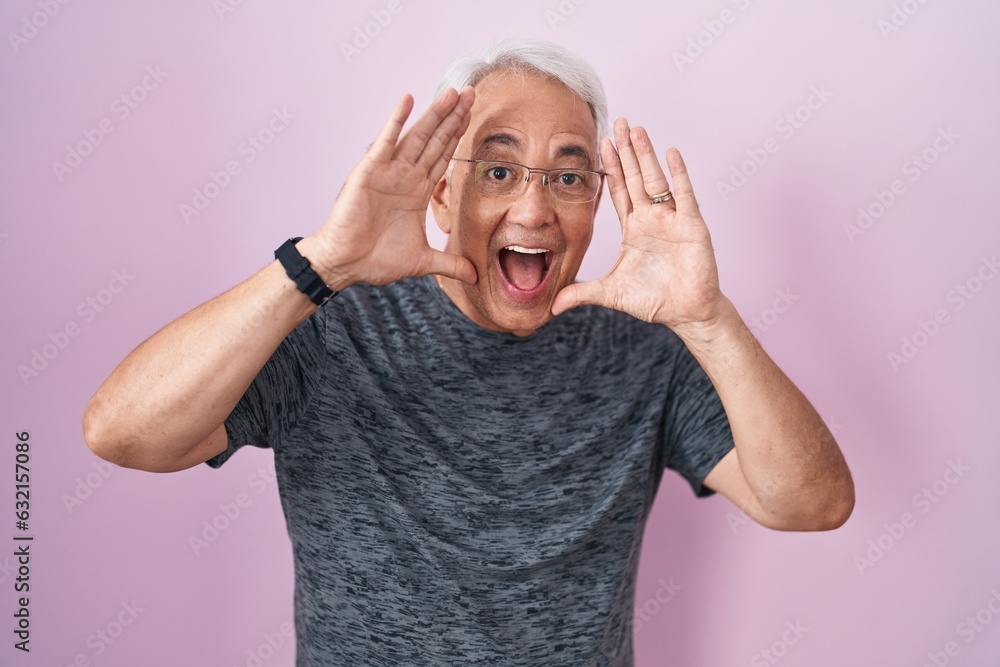 Poster middle age man with grey hair standing over pink background smiling cheerful playing peek a boo with