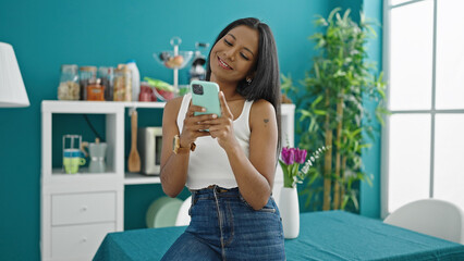 African american woman using smartphone standing at dinning room