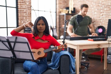 Young indian woman playing ukulele at music studio with angry face, negative sign showing dislike...