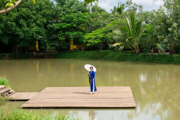 Portrait of Caucasian Woman in Ao Dai Dress walking near the small pond on the wooden bridge