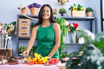 Young hispanic woman florist make bouquet of flowers at florist shop