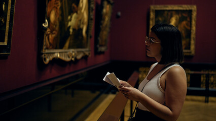 Young beautiful hispanic woman visiting art gallery reading brochure at Art Museum in Vienna