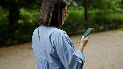 Young beautiful hispanic woman using smartphone walking at the park in Vienna