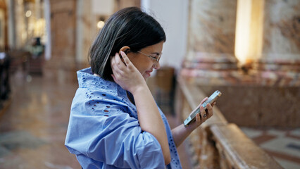 Young beautiful hispanic woman visiting church using smartphone standing at St. Karl BorromÃ¤us...