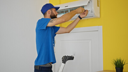 Young hispanic man technician repairing air condition machine standing on ladder at home