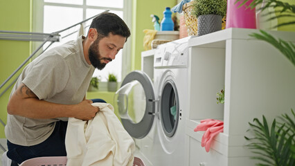 Obraz premium Young hispanic man washing clothes at laundry room