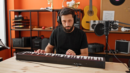 Young hispanic man musician playing piano at music studio