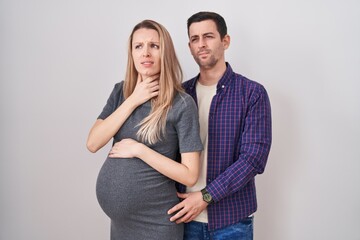 Fototapeta premium Young couple expecting a baby standing over white background touching painful neck, sore throat for flu, clod and infection