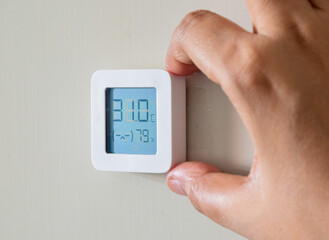 Hand holding home hygrometer and temperature indicator electronic device and fixing it on wall. Uncomfortable indoor climate.