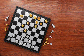 Chess board with chess pieces on wooden texture background. Chess gold with silver battle. Top view.