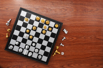 Chess board with chess pieces on wooden texture background. Chess gold with silver battle. Top view. © surasak