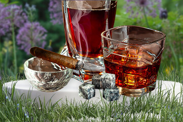 A glass of Scotch whiskey with ice and a cigar on a background of nature close-up.