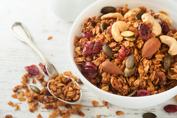 Homemade granola in glass jar with greek yogurt or milk and cashews, almonds, pumpkin with dried cranberry seeds in on white rustic wooden table background. Healthy energy breakfast or snack. Top view