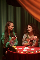 Smiling women drinking wine and discussing tarot cards spread