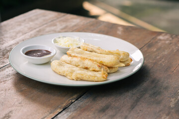 Tasty deep fried banana slices on wooden table with chocolate sauce. Popular street food in South East Asia