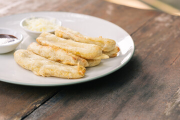 Tasty deep fried banana slices on wooden table with chocolate sauce. Popular street food in South East Asia