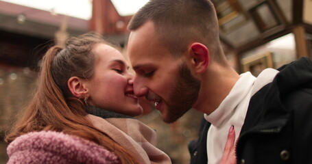 Close-up of the faces of a young couple in love kissing and hugging on the street on a gloomy autumn day. - obrazy, fototapety, plakaty