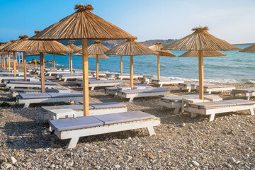 Empty beach with sun umbrellas and sunbeds in town Bar in Montenegro on Adriatic sea. Summer vacation 