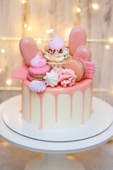Beautiful cake decorated with melted pink chocolate, macaroons, meringues, cake pops and candies on festive background