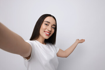 Smiling young woman taking selfie on white background, space for text