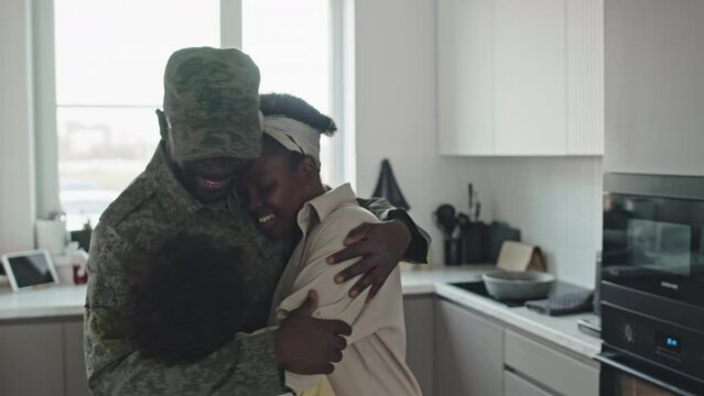 Medium shot of contented Black military man embracing his beloved wife and preteen son, returning home from army