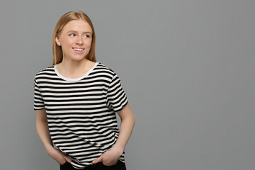 Portrait of beautiful young woman in striped t-shirt on grey background. Space for text