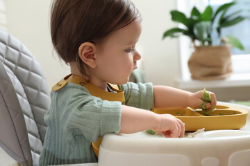 Cute little baby eating healthy food in high chair indoors