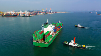  rear view of cargo container ship and tugboat sailing in sea and commercial port background to...