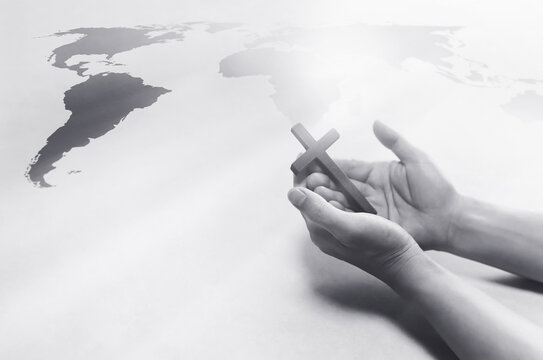 Christian holding the Holy Cross of Jesus Christ in his hand and praying for world missions, evangelism and world map background
